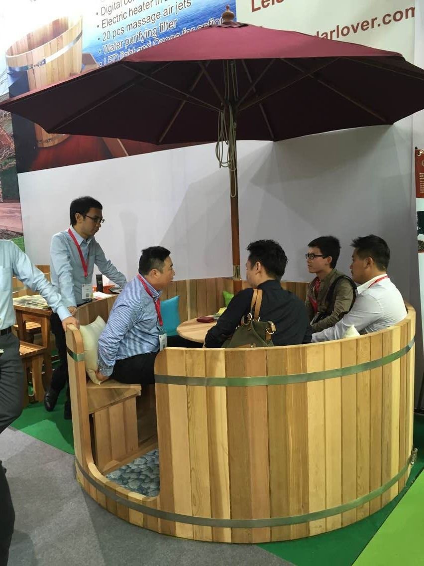 A red cedar hot tub in a trade show display area, with people sitting inside discussing something.