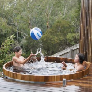 Two kids enjoying bath time play with a ball in wooden hot tub during family fun time