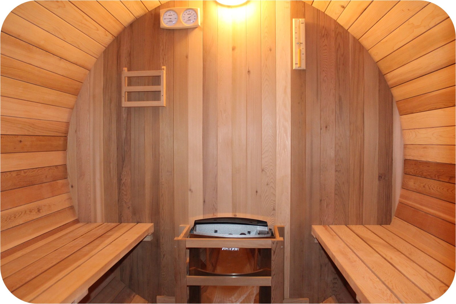 Interior of a sauna room with a Harvia electric heater, sand timer, and hygrometer under warm yellow lighting