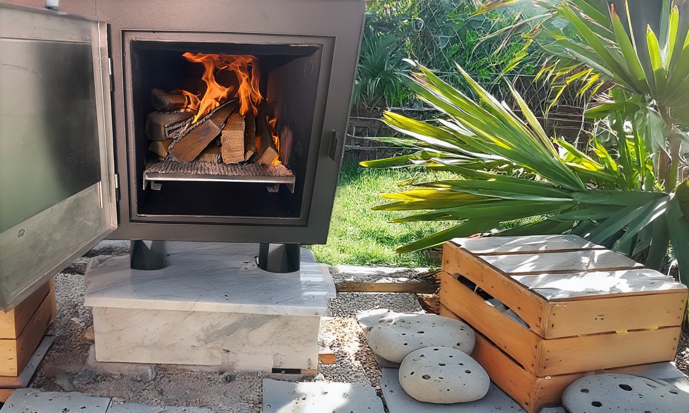 Black stainless steel wood-fired stove with open lid, showing burning wood on a silver metal rack inside