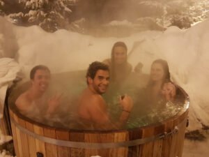 Friends enjoying relaxing spa session in red cedar wood hot tub surrounded by snow covered landscape   winter wellness retreat and social relaxation