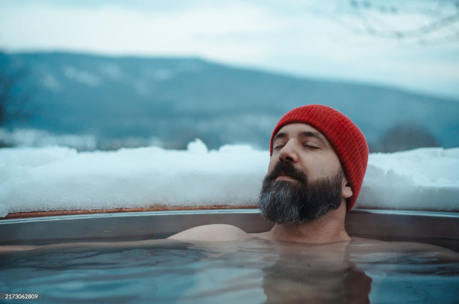 Person wearing a red hat immersed in an ice bath, with snow-covered background for cold exposure therapy.