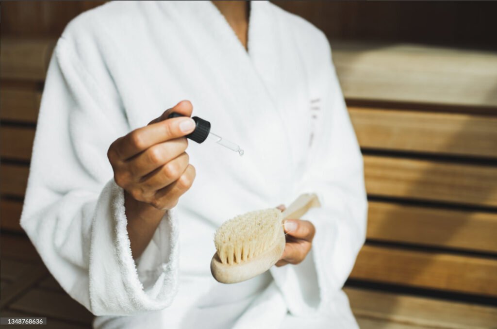 Close up of hand dripping essential oil onto a wooden body brush in sauna