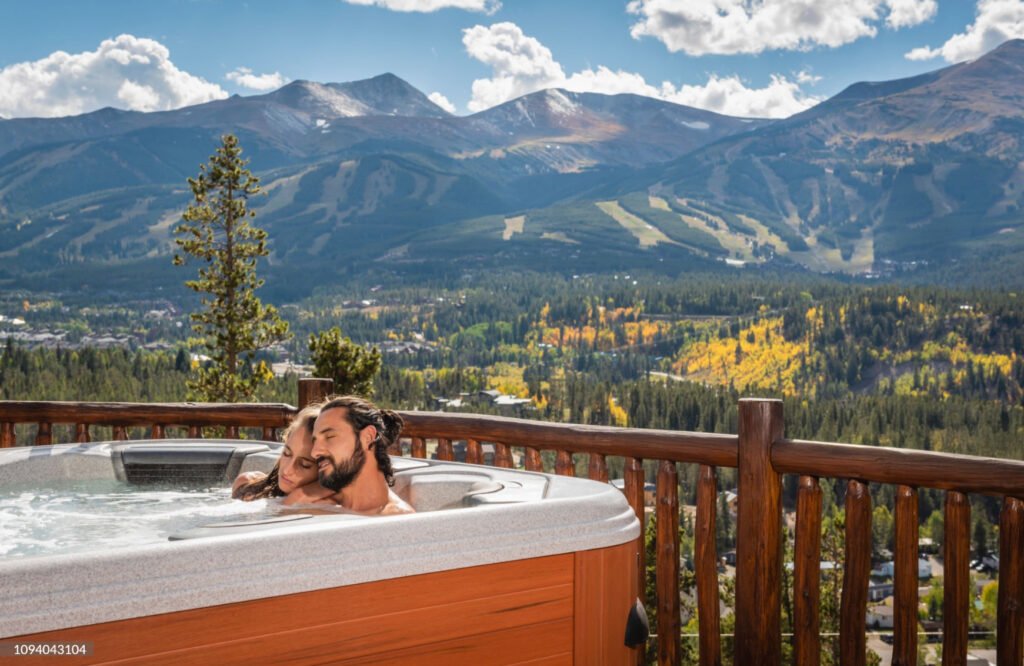 Couple enjoying a relaxing spa in a hot tub under the sunny sky, with mountains in the background.